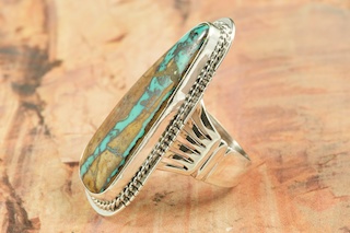 Genuine Boulder Turquoise set in Sterling Silver Ring. The cabachon is Boulder Turquoise, you can see the veins of Turquoise running through the host rock. The Boulder Turquoise Mine is located in northeast Nevada. It was discovered in 1970 by a Shoshone sheep herder. Production is small due to the remote location and winter weather. Boulder Turquoise is valued for both it's beauty and rarity. Every stone is unique. Created by Navajo Artist Lucy Valencia. Signed L. J. by the artist.